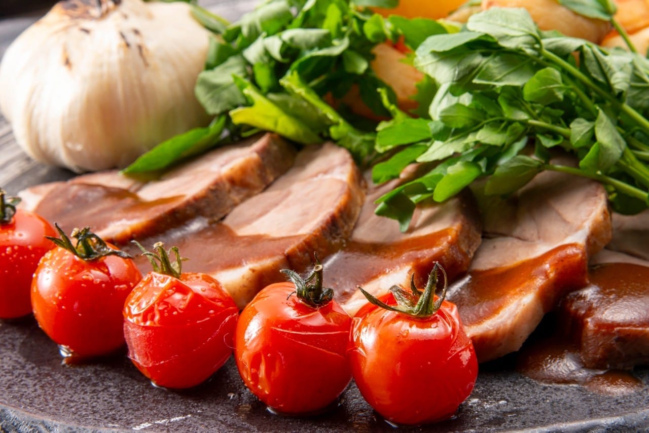 Sliced grilled duck breast plated with fresh cherry tomatoes, garlic, and parsley. Professional food photography for culinary, restaurant, and gourmet cooking content.
