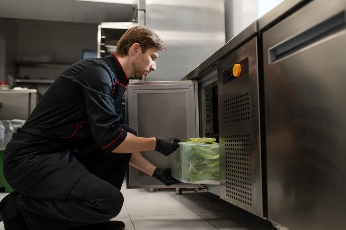 Male cook places large container of lettuce placed into refrigerator