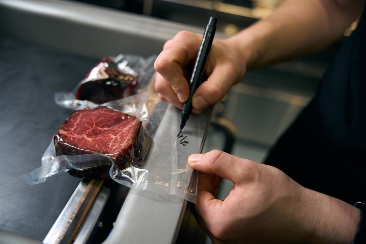 Chef man drawing date with marker on vacuum meat in refrigerator for storage
