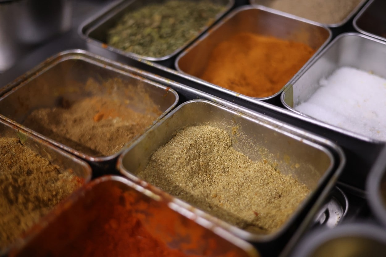 Close-up shot of various colorful ground spices stored in professional stainless steel kitchen containers.
