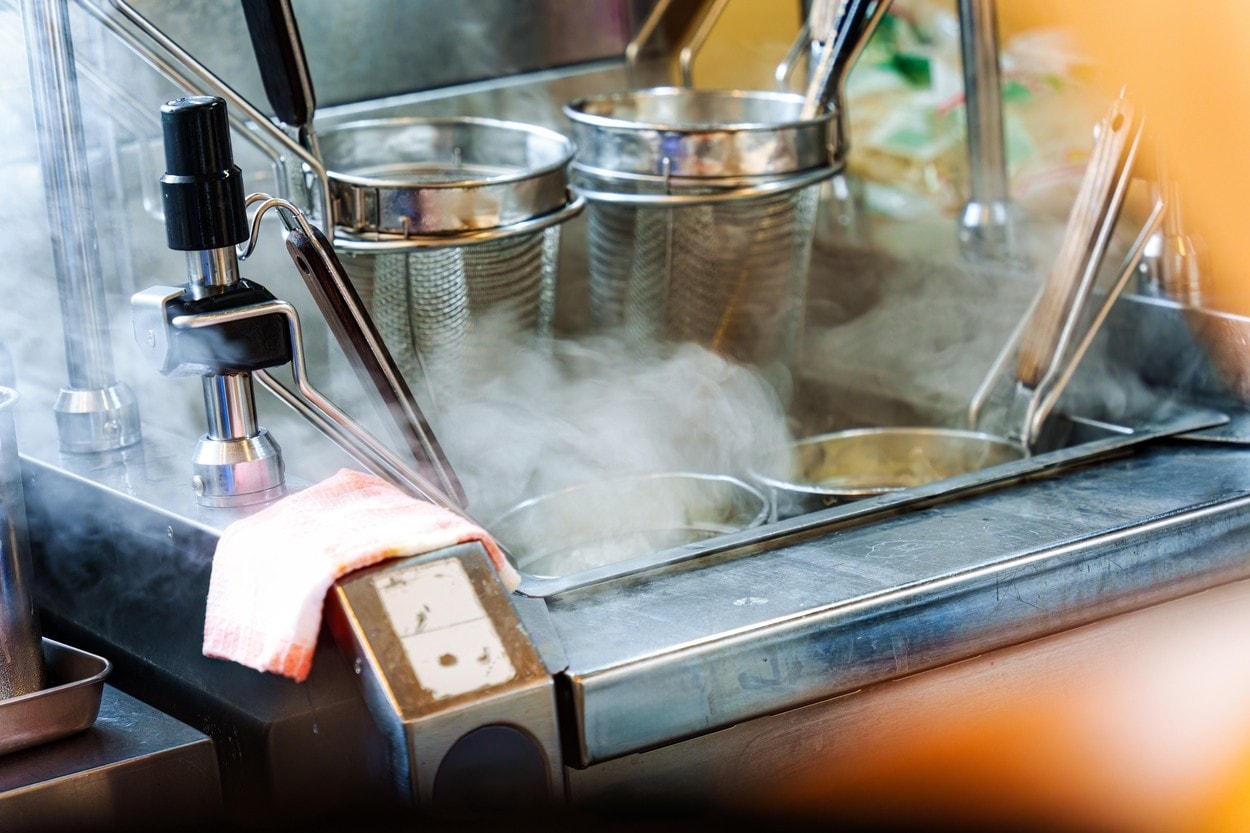 Stainless steel noodle boiling equipment with hot steam rising, used in japanese restaurant kitchen for ramen or soup preparation