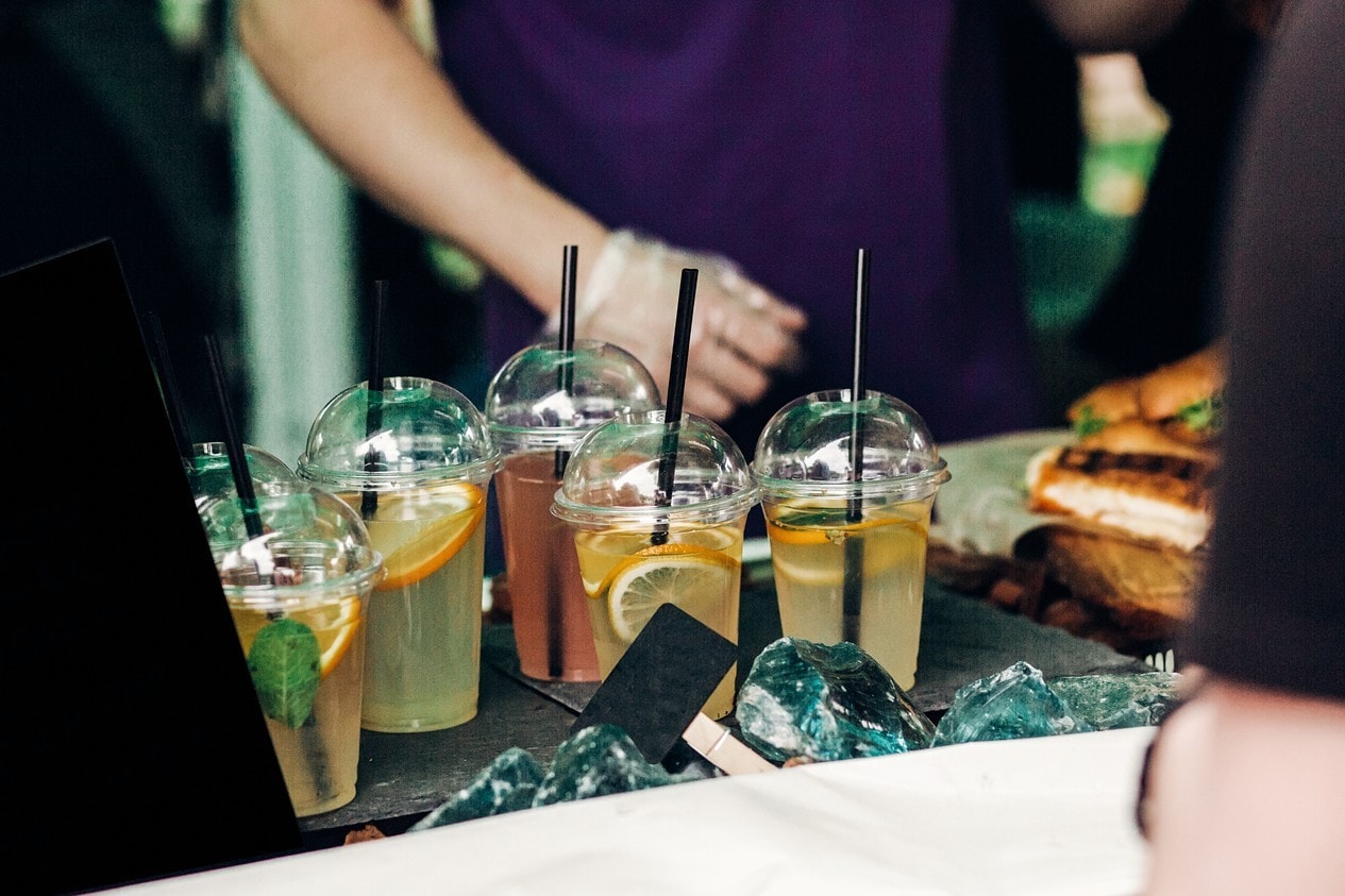 lemonade with mint and lemons on table, space for text. street food festival. drink bar at wedding reception, catering outdoors. summer picnic. cocktails in plastic cups with straws