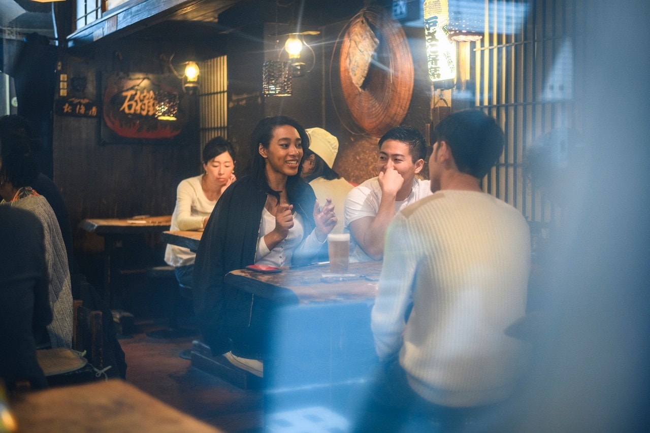 Young friends in their 20s sitting inside an izakaya in Tokyo enjoying conversation and drinks on the weekend.