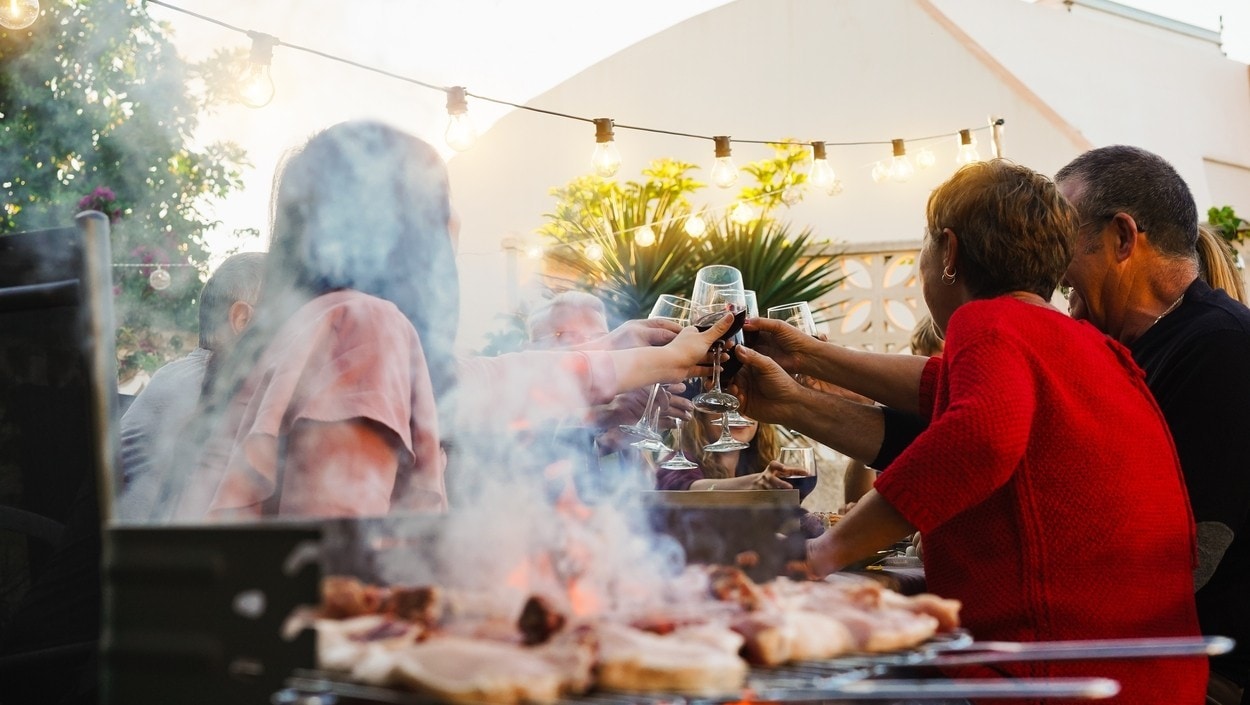 Group of friends having fun at barbecue dinner cheering with red wine - Food, friendship, and summer people lifestyle concept - Focus on hands clincking