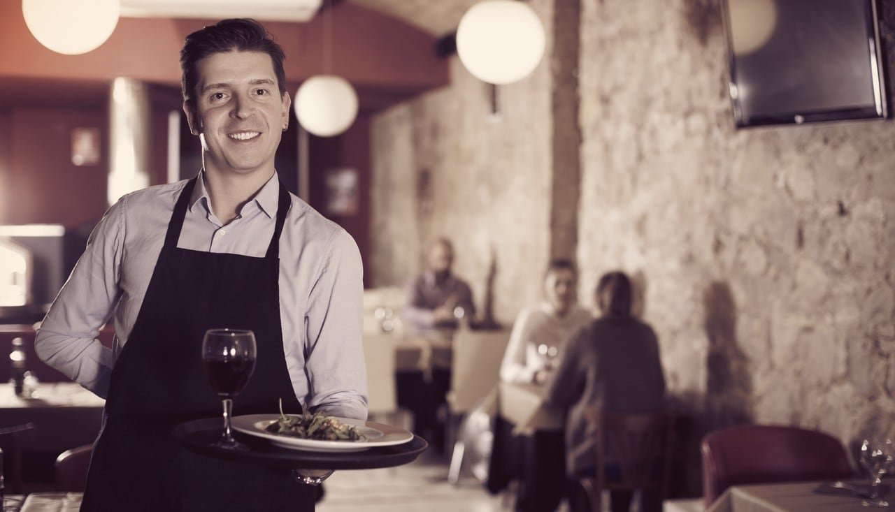 Handsome waiter with serving tray welcoming to restaurant