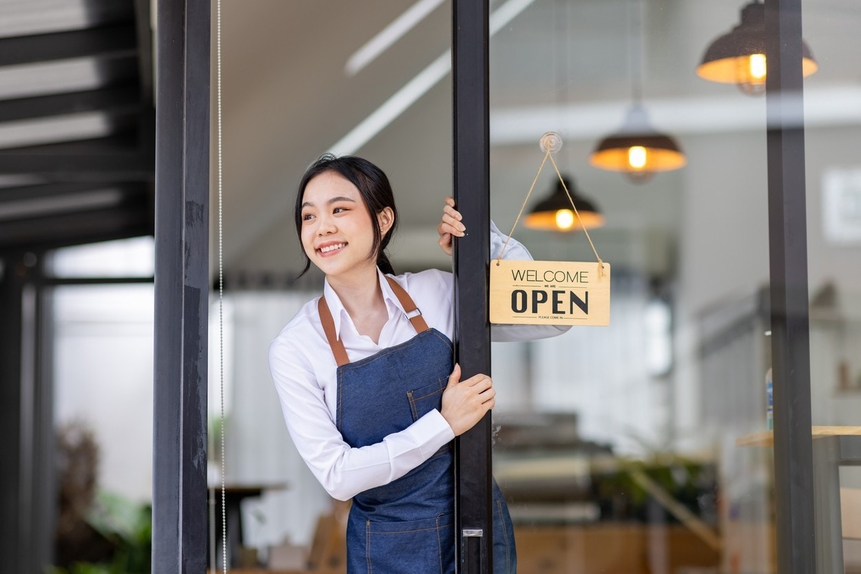 Startup successful small business owner sme beauty girl stand with tablet smartphone in coffee shop restaurant. Portrait of asian tan woman barista cafe owner. SME entrepreneur seller business concept