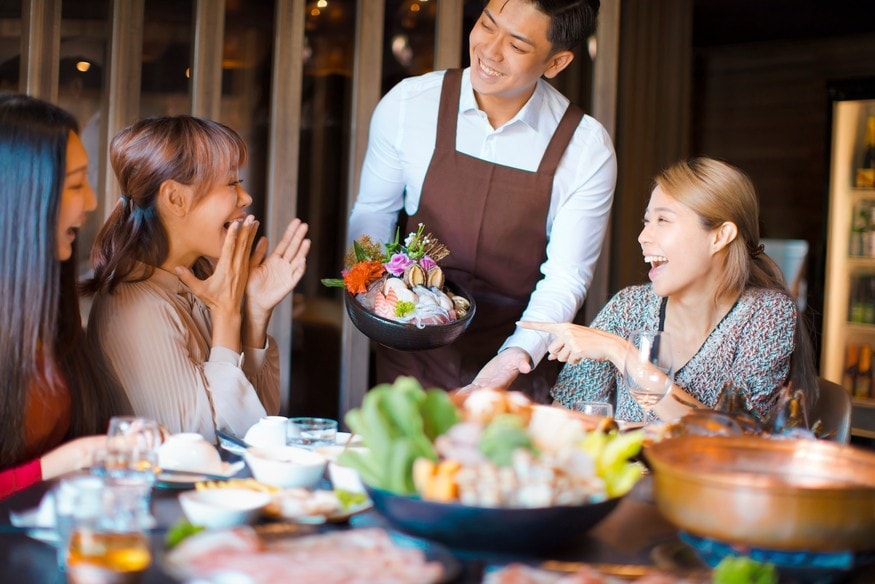 Happy waiter  bring  seafood  and serving group of friends in restaurant.