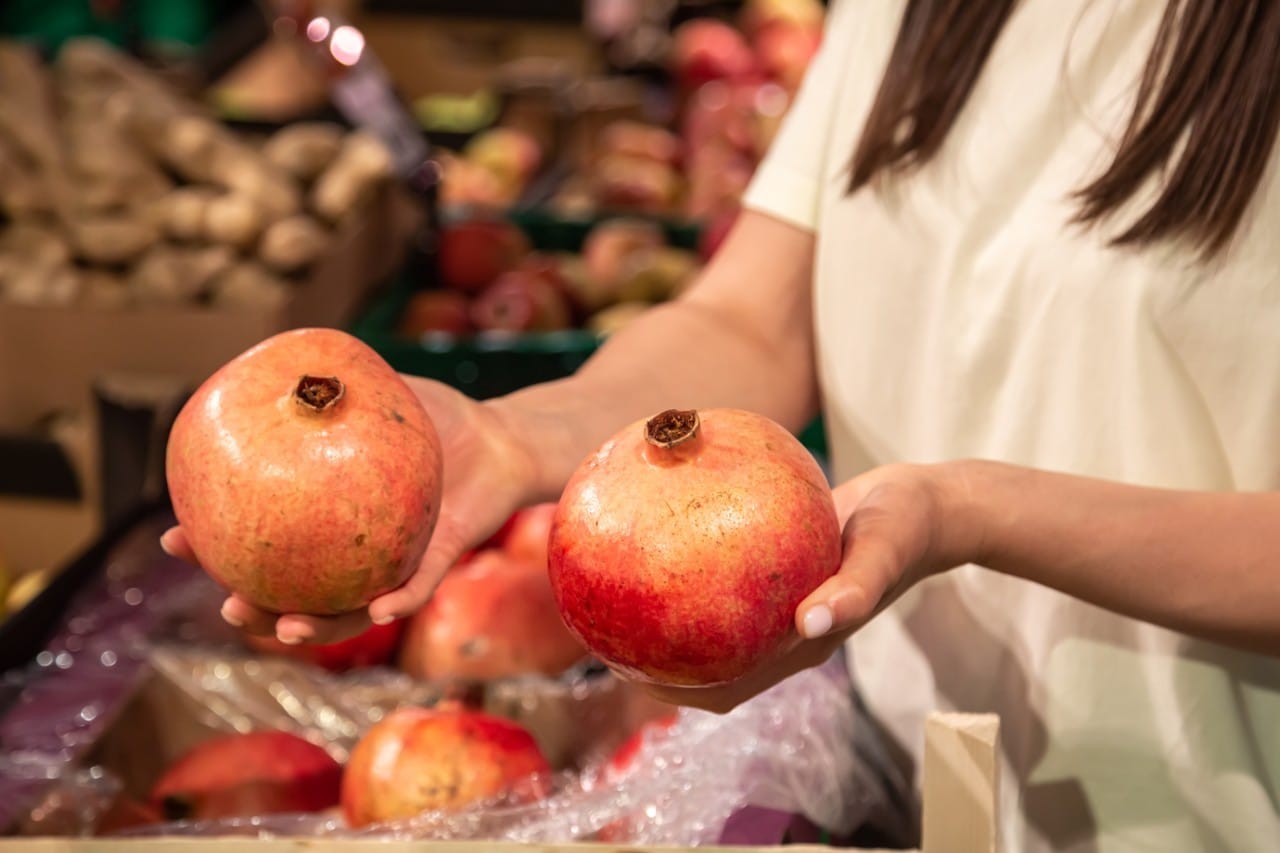 The woman customer holds pomegranate in the store or in the market. Juicy and fresh fruits.