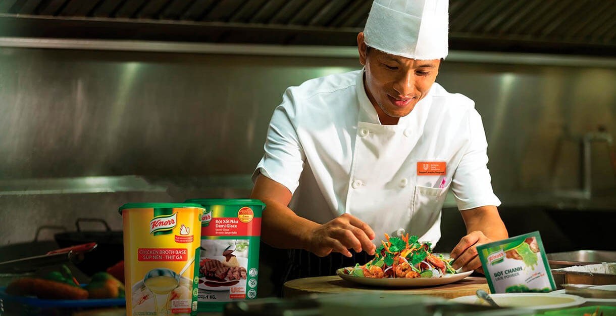 Asian chef serving a salad in his kitchen with Knorr product placing around Asian chef serving a salad in his kitchen with Knorr product placing around